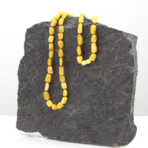 Csodálatos vajszínű sárga borostyán nyaklánc kőből készült bemutató állványon.